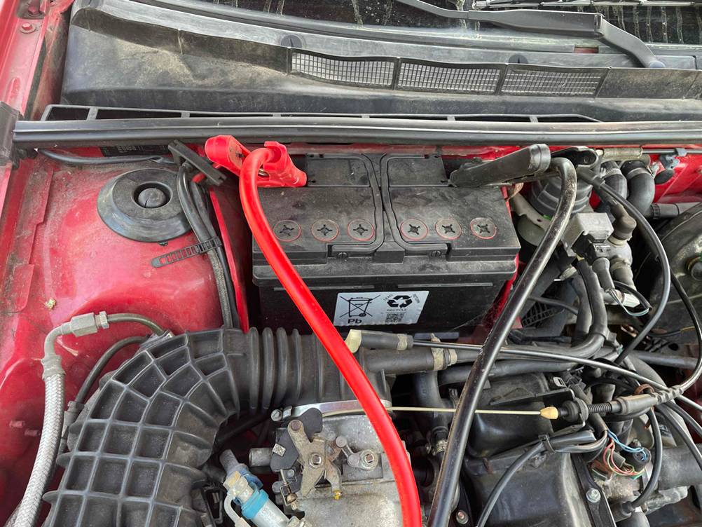 Starthilfekabel getestet: Nahaufnahme des angeschlossenen Kabels an eine Batterie im Motorraum.