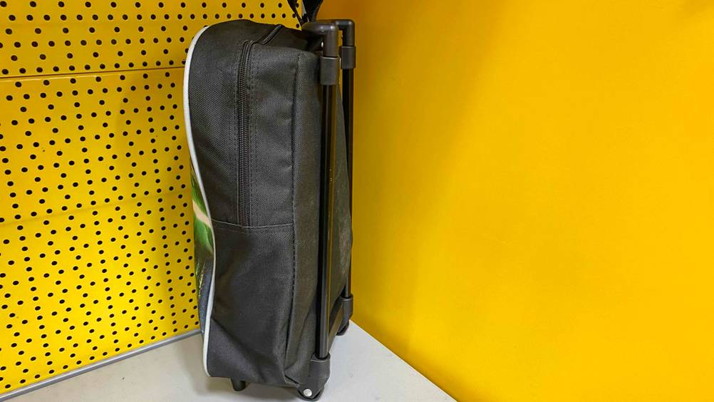 Seitenansicht auf einen geschlossenen getesteten Kindertrolley aus schwarzem Gewebe vor gelber Wand.