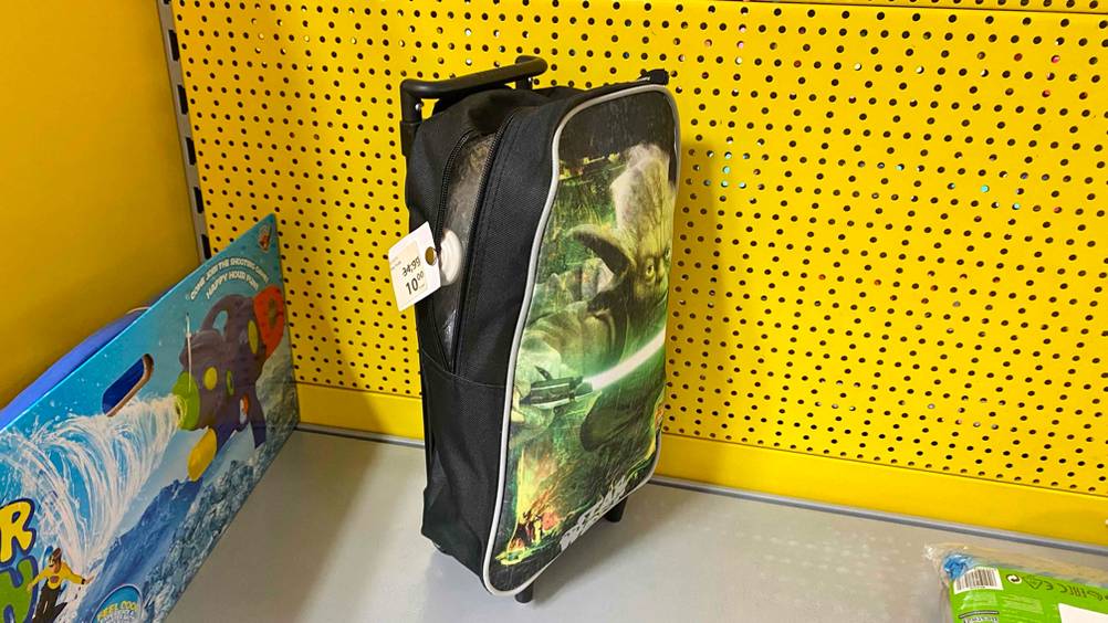 Seitliche Ansicht auf einen Starwars Kindertrolley im Test mit geöffnetem Reißverschluss vor gelber Wand und neben bunter Tüte.
