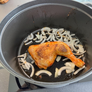 Im Behälter des Staub Cocotte 1007460 liegen ein Stück Fleisch und Zwiebeln während des Bratens auf dem Herd