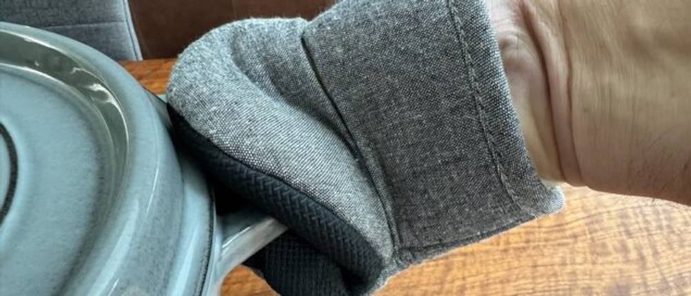 Eine Hand hält den Griff des Staub Cocotte 1007460 mit einem Handschuh fest