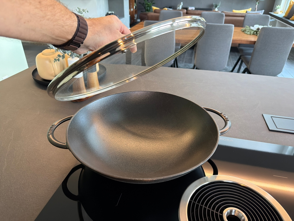 Eine Hand nimmt den Deckel vom Staub-Wok
