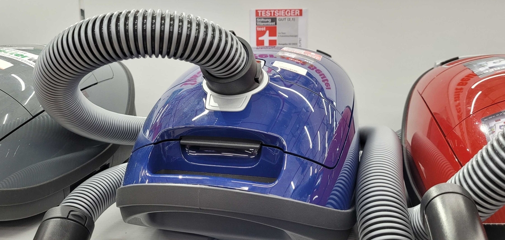 Ein Staubsauger mit Beutel steht zwischen anderen Geräten in einem Verkaufsregal.