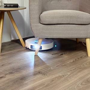 Der Staubsaugerroboter fährt unter einem Sessel.