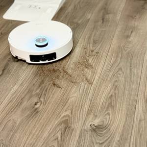 Der Staubsaugerroboter fährt über einen Laminatboden und saugt Dreck auf.