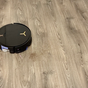 Ein schwarzer Staubsaugerroboter saugt Staub auf einem grauen Laminatboden auf.