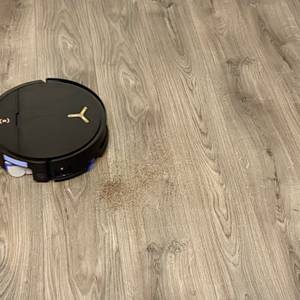 Ein schwarzer Staubsaugerroboter saugt Staub auf einem grauen Laminatboden auf.