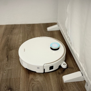 Der Staubsaugerroboter steht vor einer weißen Wand.