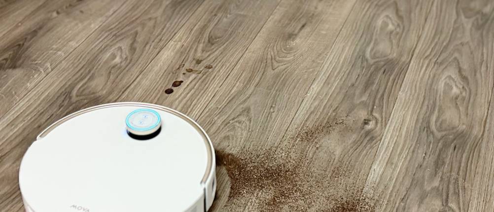 Der Staubsaugerroboter fährt über einen Laminatboden und saugt Dreck auf.