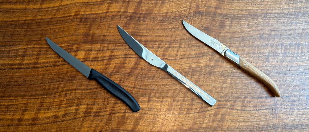 Drei Steakmesser liegen nebeneinander auf einem Holztisch