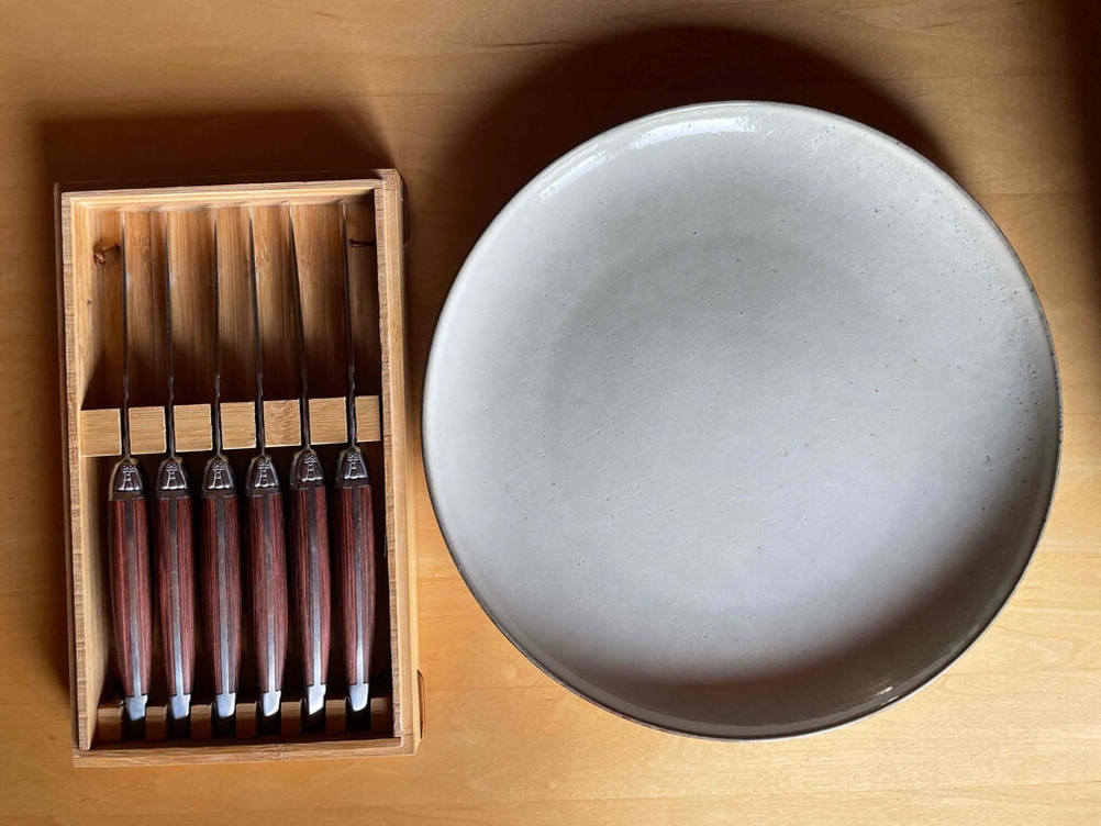 Steakmesser Test: Ein Holzkasten mit sechs Steakmessern neben einem Teller auf einem Holztisch.