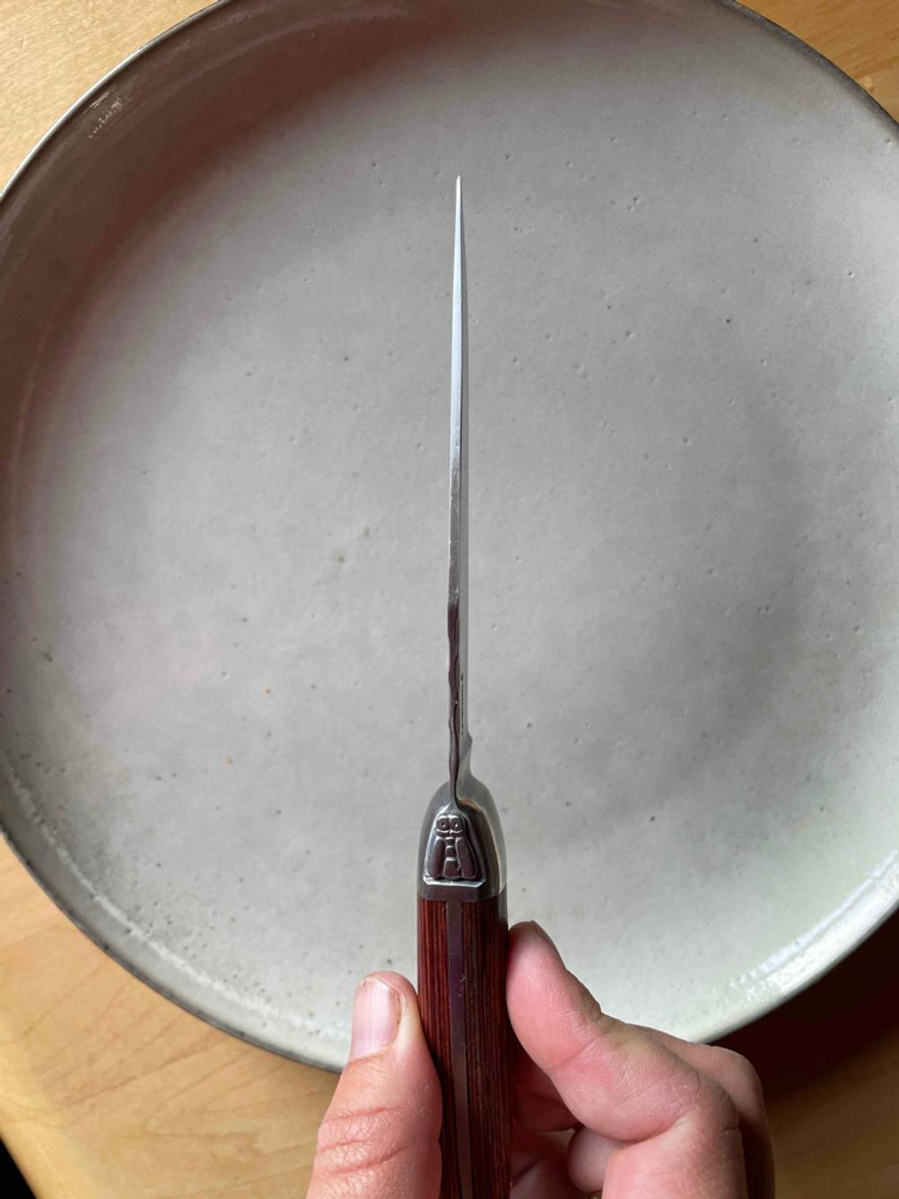 Steakmesser Test: Nahaufnahme auf die Klinge von oben eines Steakmessers von einer Hand über einen Teller gehalten.