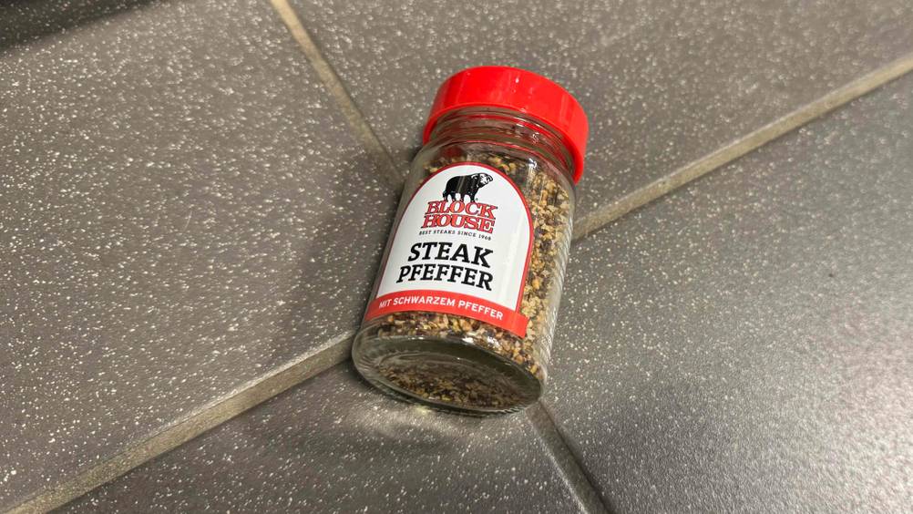 Auf einem grauen Boden liegt ein Glas des getesteten Steakpfeffers.