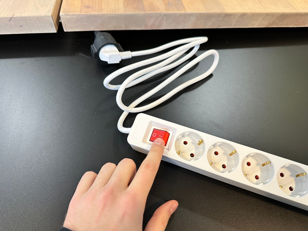 Eine Hand betätigt den roten Kippschalter der Hama-Steckdosenleiste.