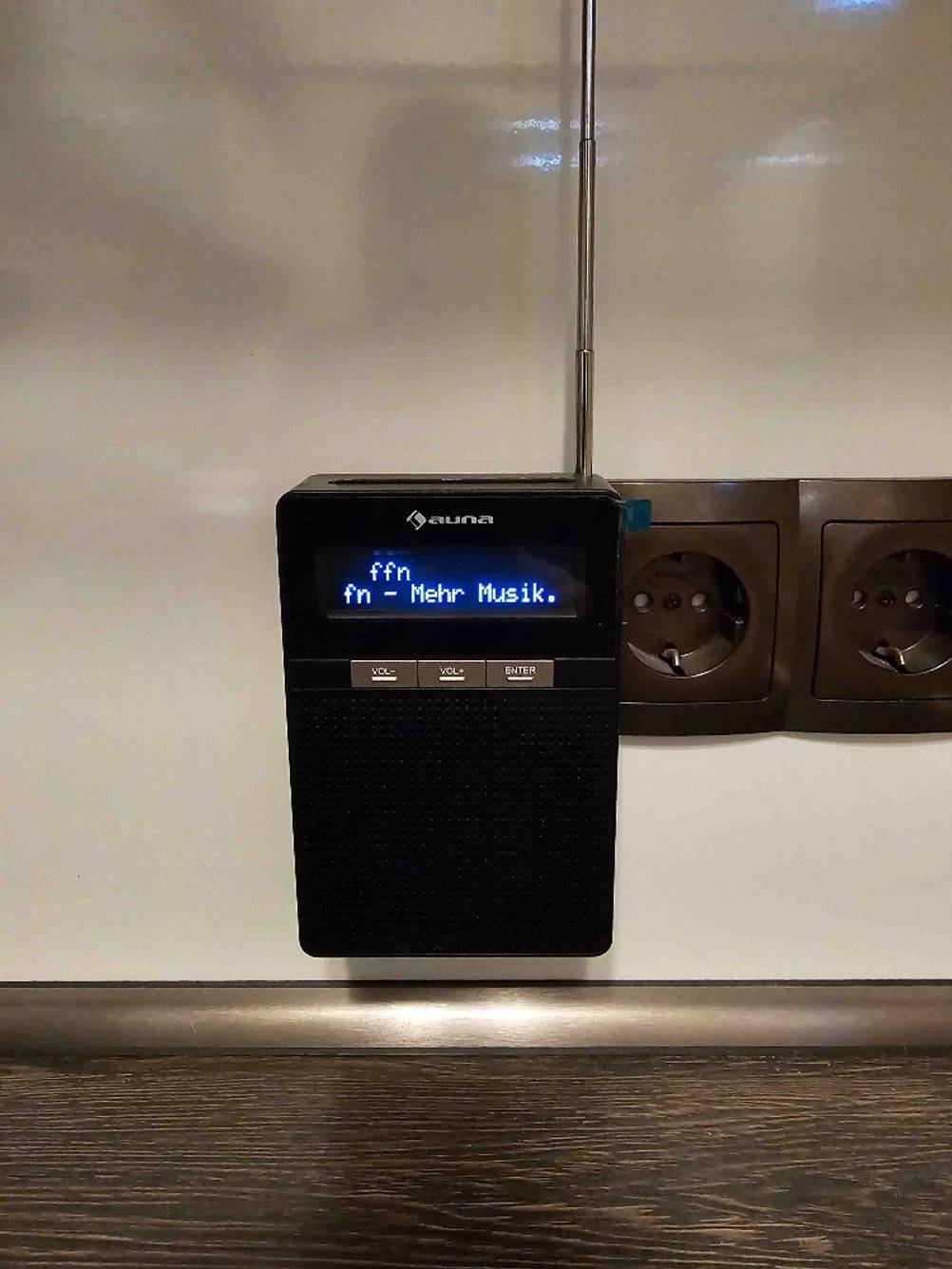 Das getestete Steckdosenradio, angeschalten, von vorne in der Dose steckend.