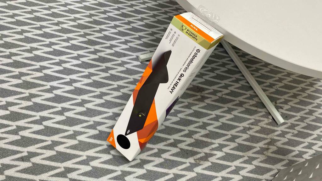 Die weiß-orangefarbene Verpackung eines Steelseries XXL-Mauspads im Test lehnt an einer weißen Ausstellungsfläche im Geschäft.