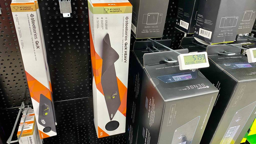XXL-Mauspads im Test: eine weiß-orangefarbene Verpackung hängt neben weiteren verpackten Mauspads an einem Verkaufsstand.