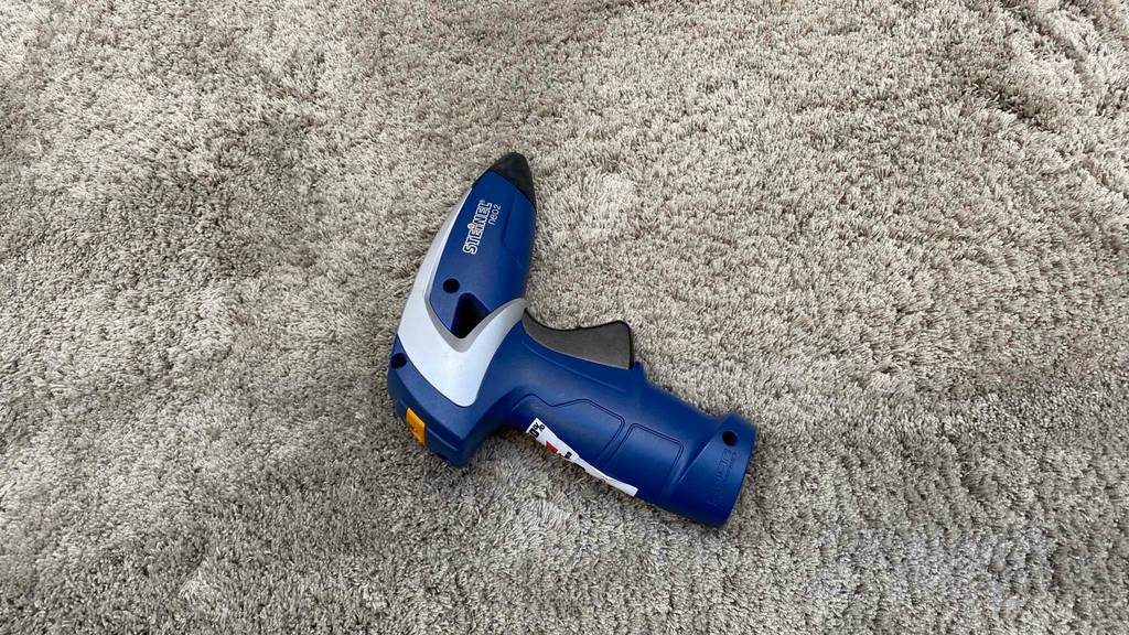 Akku-Heißklebepistole getestet: Ein Gerät liegt auf der Seite auf einem grauen Teppich.
