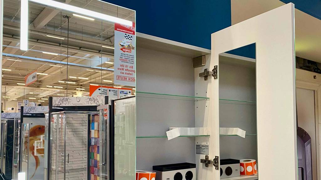 Im Test: Bad Spiegelschrank mit Beleuchtung in Weiß, mit geöffneter rechter Tür inklusive Innenspiegel, in einem Verkaufsbereich.