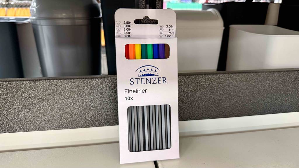 Eine weiße 10-Stück-Packung mit Finelinern im Test lehnt an einem Regal im Verkaufsbereich.