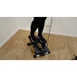 Eine Person führt eine Stepp-Bewegung auf dem Gerät aus und trainiert gleichzeitig mit Widerstandsbändern.