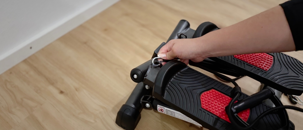 Eine Hand, die einen Federring zieht, um die Höhe eines Pedals eines Mini-Steppers einzustellen.