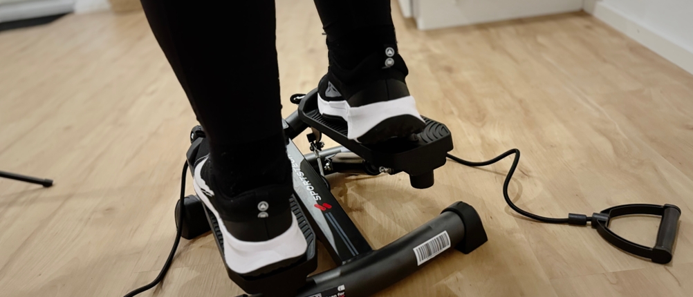 Eine Nahaufnahme von Füßen in Turnschuhen, die einen Mini-Stepper mit Widerstandsbändern benutzen.