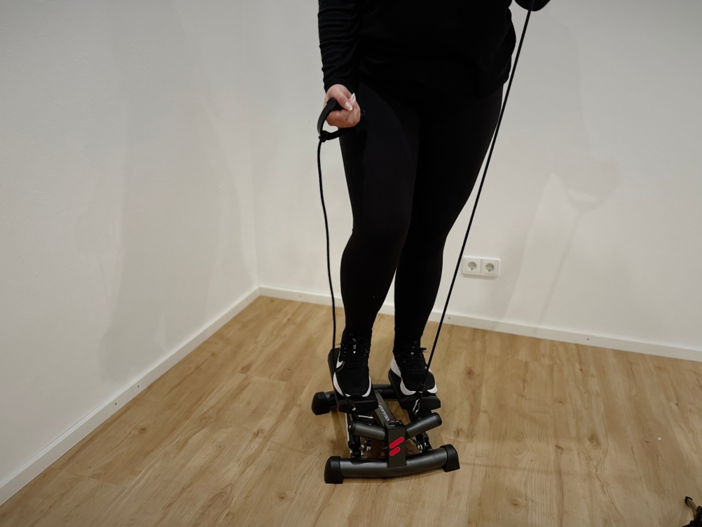 Eine Person, die auf einem Mini-Stepper trainiert und dabei die Griffe der Widerstandsbänder hält.