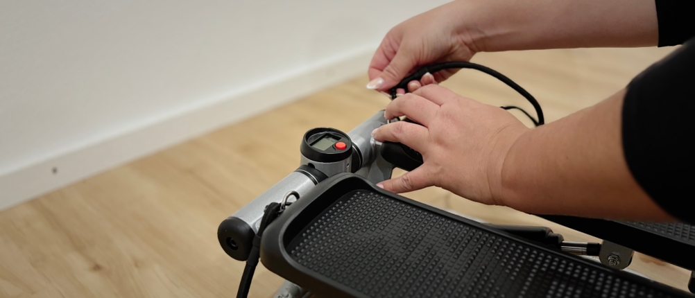 Zwei Hände bedienen das Digitaldisplay und das Widerstandsseil eines Mini-Steppers.