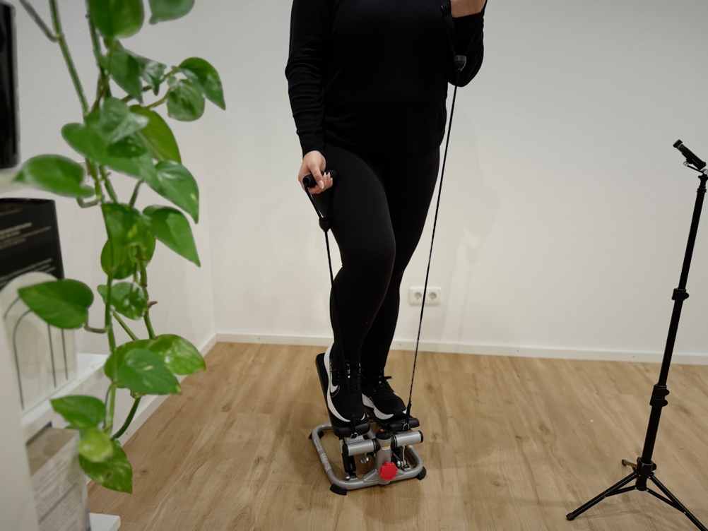 Eine Person in schwarzer Trainingskleidung trainiert auf einem Mini-Stepper und hält die Widerstandsseile fest.