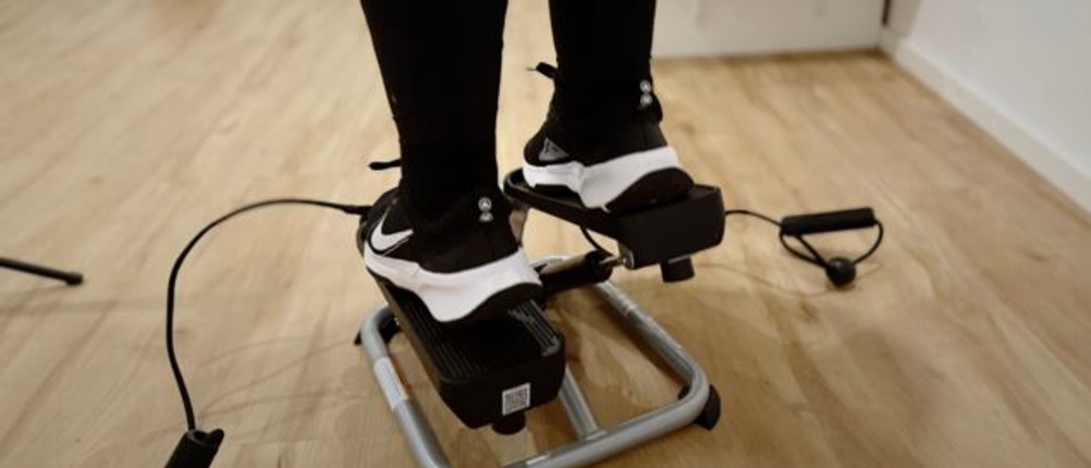 Ein Paar Füße in schwarzen und weißen Turnschuhen auf einem Mini-Stepper mit Widerstandsseilen.