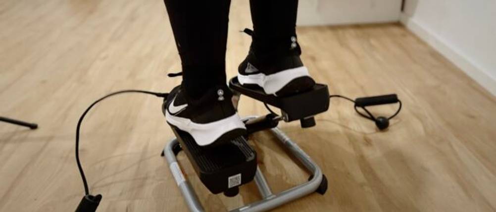 Ein Paar Füße in schwarzen und weißen Turnschuhen auf einem Mini-Stepper mit Widerstandsseilen.