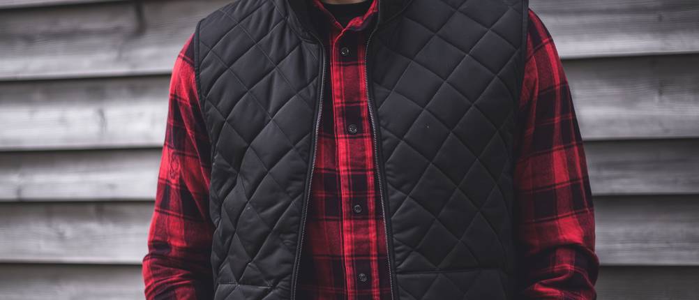 Steppweste-Herren-Test: Mann trägt schwarze Steppweste über rotkariertem Holzfällerhemd.