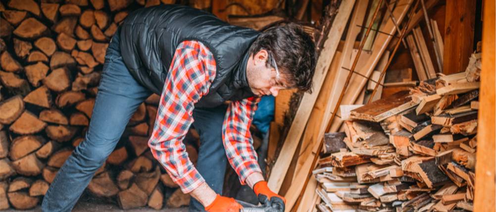 Steppweste für Herren im Test: Mann mit Steppweste und Karohemd arbeitet im Holzlager.