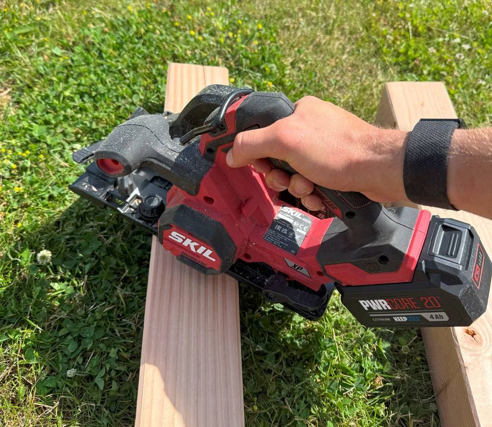 Eine Person hält eine Stichsäge auf einen Holzpfosten.
