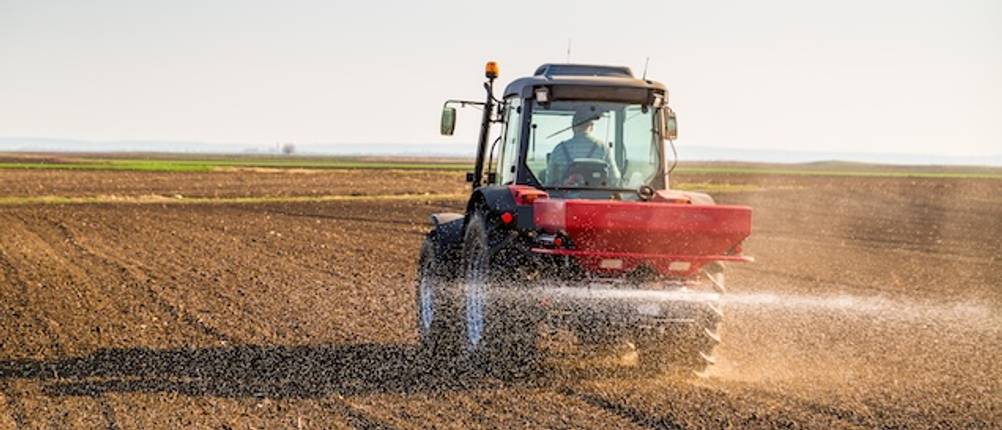 Stickstoffdünger im Test: Ein roter Traktor mit Streumaschine bringt auf einem Acker Dünger aus.