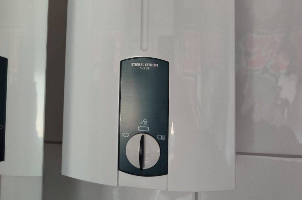 Stiebel Eltron DHB ST Durchlauferhitzer im Test: Das Gerät inklusive weißem Temperaturwahl-Schalter befindet sich an einer hellen Fliesen-Wand.