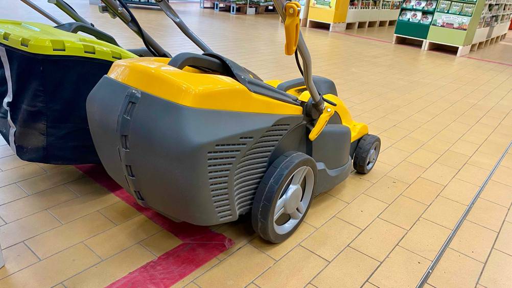 Elektro-Rasenmäher-Test: ein gelb-schwarzes Stiga Modell inklusive Mulchfunktion und klappbarem Griff steht neben einem anderen Markenprodukt auf einem beigefarbenen Fliesenboden im Verkauf.