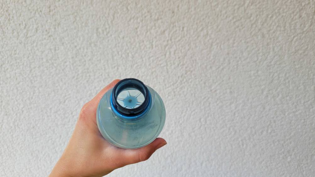 Stilles Mineralwasser-Test: Nahaufnahme der Flaschenöffnung, die eine Hand vor eine helle Wand hält.