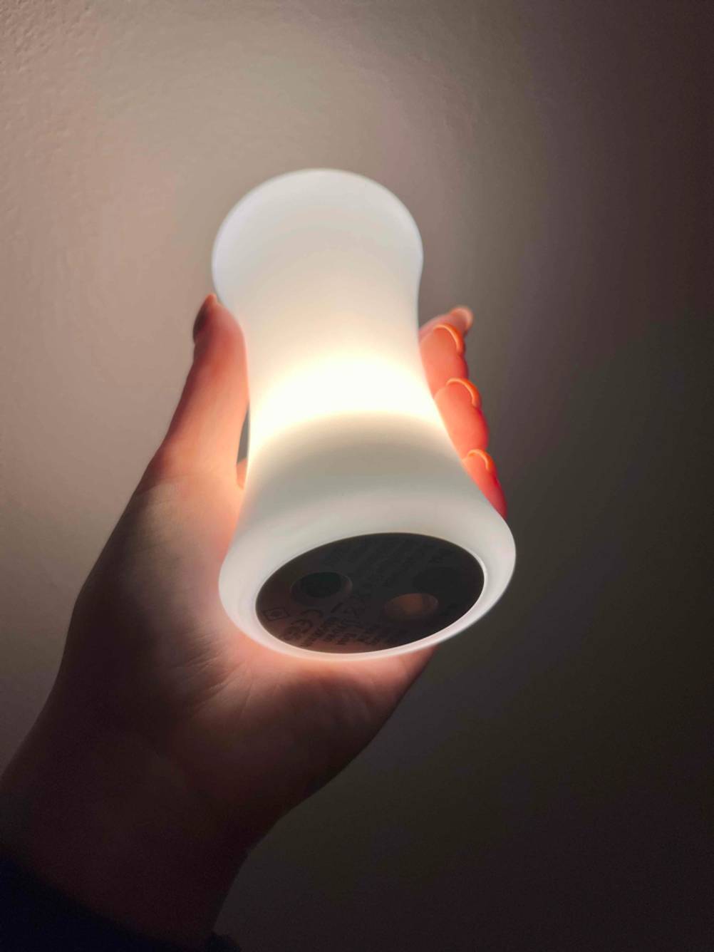 Hand hält im Dunkeln das leuchtende weiße Stilllicht im Test mit Fokus auf die Basis mit Aufladevorrichtung.