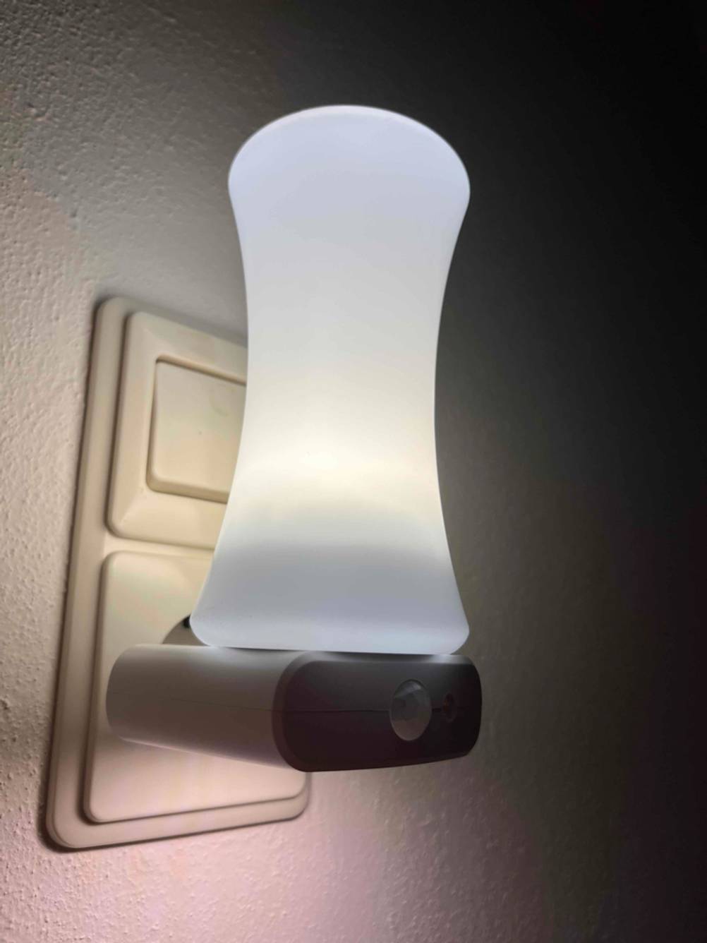 Eingeschaltetes weißes Stilllicht im Test befindet sich auf einem leuchtenden Aufladegerät, der in einer Steckdose unter einem Lichtschalter steckt.