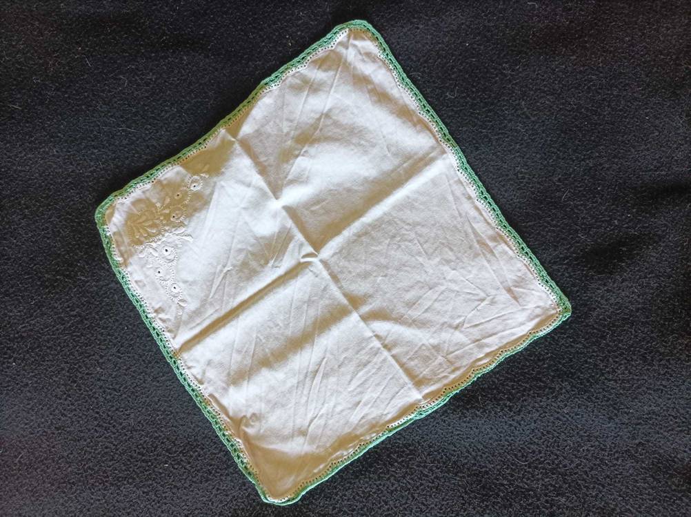 Ein weißes Stofftaschentuch im Test mit grünem Rand auf einer schwarzen Decke.