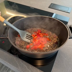 Mit einem Pfannenwender werden Paprikastücke im Stoneline Cocotte mit Hackfleisch gemischt