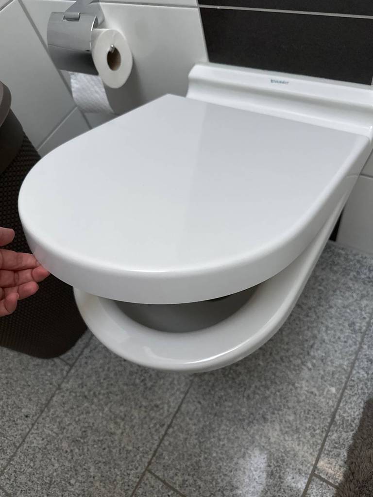 Hand hebt weißen, getesteten WC-Sitz mit Absenkautomatik an.