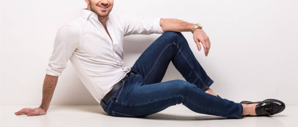 Stretch-Jeans-Herren-Test: Mann in weißem Hemd und blauer Stretch-Jeans sitzt auf dem Boden.