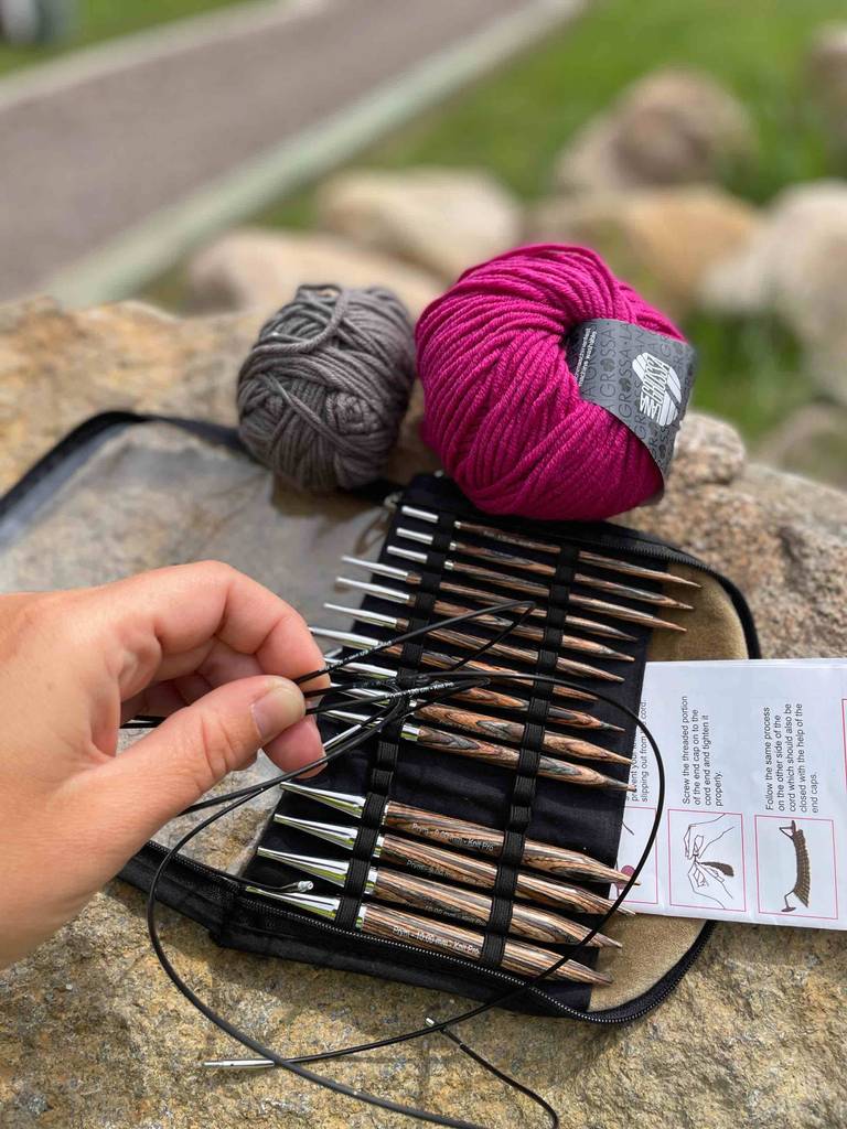 Eine Hand hält mehrere Rund-Stricknadeln im Test über eine Aufbewahrungstasche mit weiteren Stricknadeln.