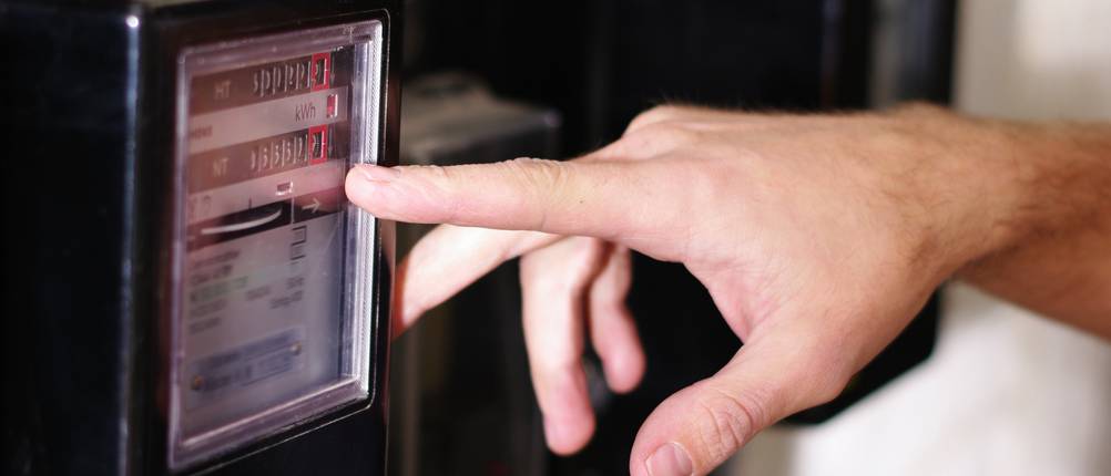 Test verschiedener Anbieter von Strom: Ein Mann zeigt mit seinem Finger auf einen Stromzähler.