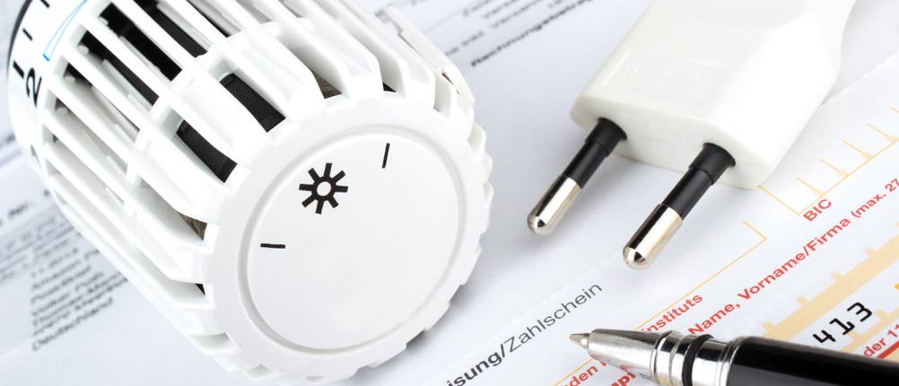 Strom- und Gas-Kombitarife im Test: Auf einem Überweisungsschein liegt sowohl der Drehknopf einer Heizung als auch der Stecker eines Stromkabels.