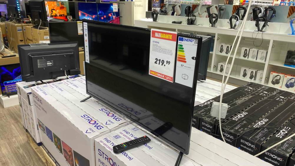 Ein getesteter 40-Zoll-Fernseher steht in einer Verkaufsfläche auf mehreren Verpackungskartons im Hintergrund Kopfhörer.