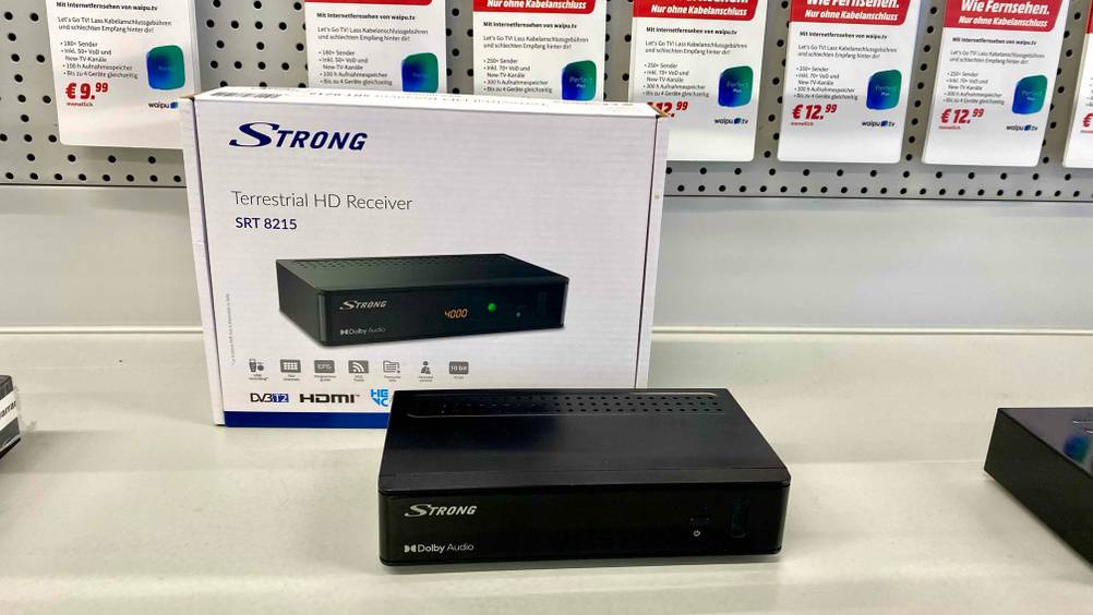 Im Test: Ein Receiver steht vor seiner Verpackung auf einer hellen Fläche im Hintergrund Infokarten.